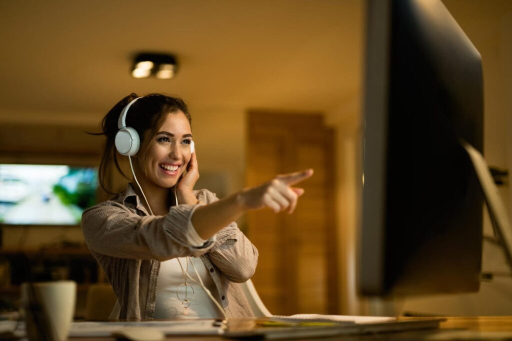 happy woman with headphones pointing computer screen while surfing net evening home