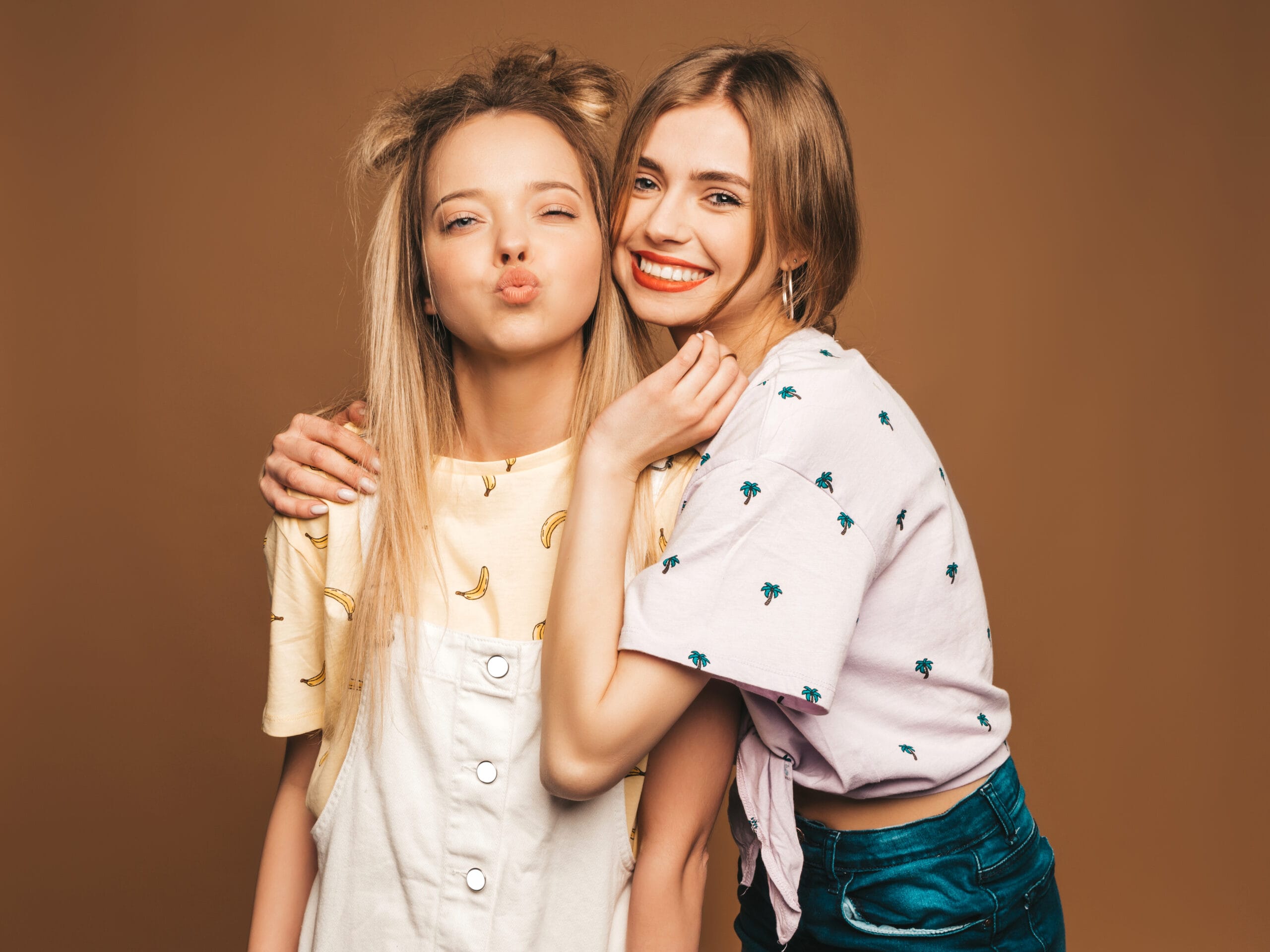 two young beautiful smiling blond hipster girls trendy summer colorful t shirt clothes sexy carefree women posing beige background positive models giving kiss scaled 1